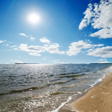 Mavi gökyüzünde güneş, denizin üzerinde bulutlar.