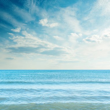 Gün batımında mavi denizin üzerinde bulutlarla karanlık gökyüzü