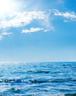 Mavi gökyüzünde güneş, deniz üzerinde bulutlar.