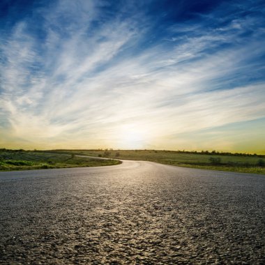 Mavi gökyüzünde asfalt yolda gün batımı. yumuşak odak