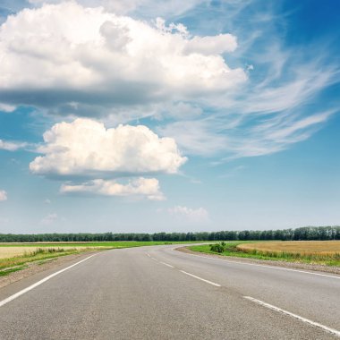 Ufka giden asfalt yol ve üzerinde bulutlar olan mavi gökyüzü.