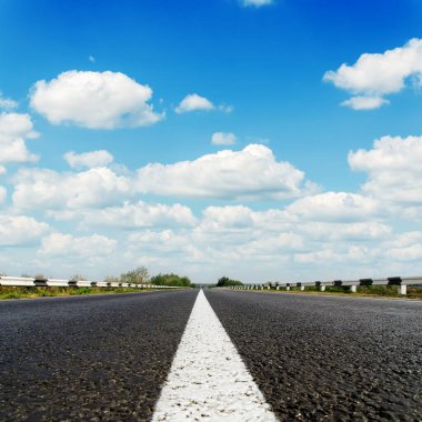 Ortasında beyaz çizgi olan siyah asfalt yol ve üzerinde bulutlar olan mavi gökyüzü.