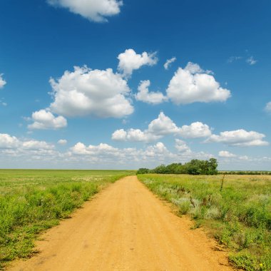 Kırmızı kirli yol, yeşil tarlalarda, derin mavi gökyüzünün altında bulutlarla.