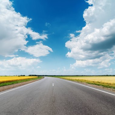 Mavi gökyüzünde bulutların altında asfalt yol