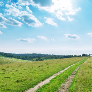 Dağlarda yol, bulutlar ve güneş olan yeşil çayır.