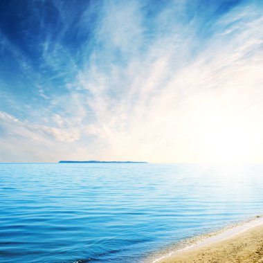 Adalı mavi deniz ve gün batımında bulutların altında sarı kum