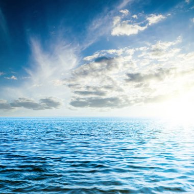 Mavi denizin üzerinde alçak kara bulutlarda gün batımı