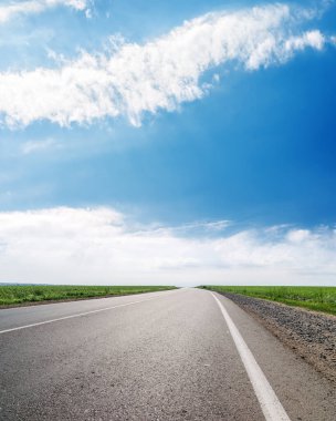 Ufukta asfalt yol ve mavi gökyüzünde beyaz bulutlar
