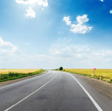 Arazide asfalt yol ve bulutlu ve güneşli mavi gökyüzü