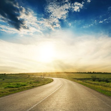 Gün batımında ufka giden yol. Asfalt yolu üzerinde güneşli alçak bulutlar