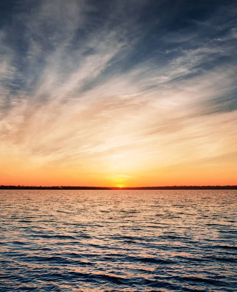 暗い水の上の低い劇的な雲の中のオレンジ色の夕日 — ストック写真