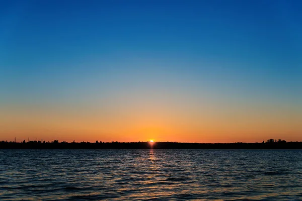 川の暗い水とそれ以上の日の出 最初の太陽が澄んだ空に川を渡り — ストック写真
