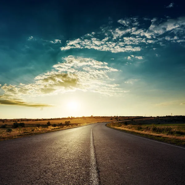 Asfalt yolda, gün batımında, dramatik bulutlarda alçak güneş