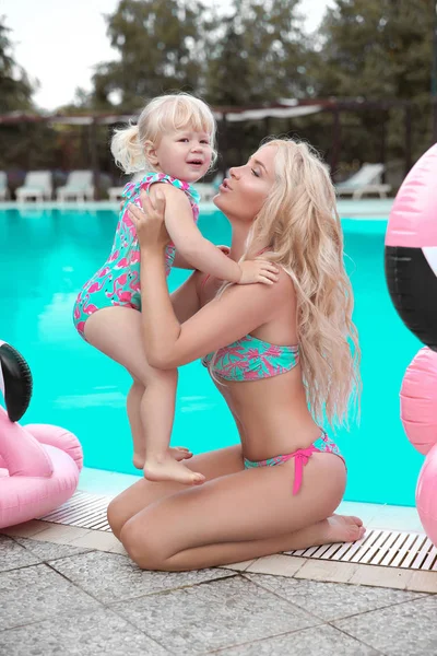 美女时尚妈妈带着女儿的家人看 美丽的金发女人与小漂亮吉尔的乐趣穿着游泳在寒冷的海滩上的泳池摆姿势 暑假假期 — 图库照片