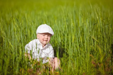 Beyaz şapkalı komik küçük çocuk sakin yaz Park yeşil çim.