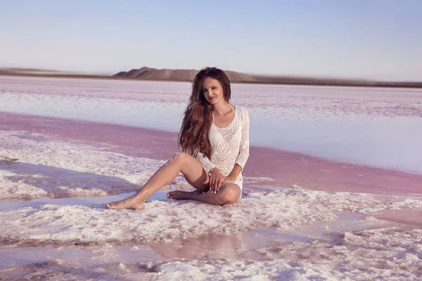 美丽的自由性感女孩白色泳装坐在咸海滩日落 皮肤黝黑的女人 长的健康的头发摆在盐粉红色的湖泊 享受自然景观 豪华夏日假期 — 图库照片