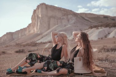 Yaşam tarzı açık havada dikey genç şık hippi kız trendy kıyafeti beyaz rock gemisi günbatımında poz. Kadın moda kavramı. Moda model giysili güzel iki ikiz. Yaz tatili.