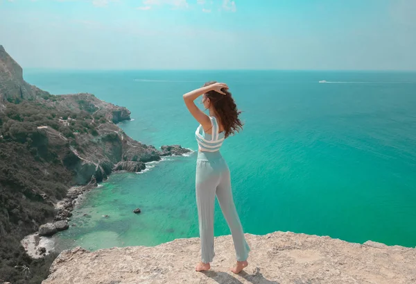 Summer beach fashion woman outfit. Beautiful traveller girl having fun on cliff mountains enjoying lagoon bay. Summertime vacation lifestyle.