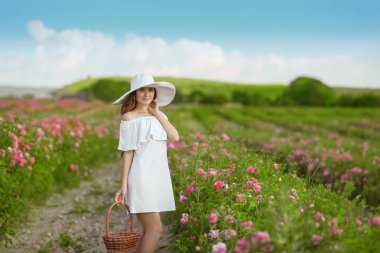 Bahar çiçeği pembe gül bahçe üzerinde poz sepeti tutan uzun kıvırcık saçlı beyaz şapkalı güzel ve genç birbayan. Çekici çekici esmer kadın açık portre.