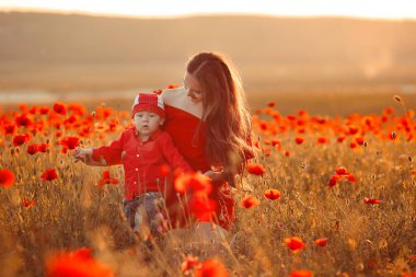 Gün batımında hayattan zevk haşhaş oğlu ile annesi. Mutlu aile yaz tatili. Güzel esmer uzun sağlıklı saç küçük çocuk holding ile. Kırmızı alanın üzerinde kaygısız Genç Anne. Kırsal manzara.