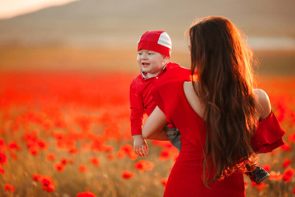 Mother with son in poppies enjoying life at sunset. Happy family summer vacation. Pretty brunette with long healthy hair holding little boy. Carefree young mom over red field. Countryside landscape.