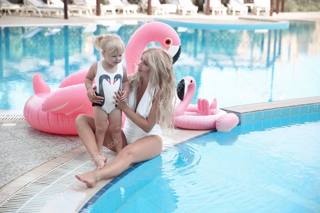 Beauty fashion mother with daughter family look. Beautiful blonde pretty woman having fun with adorable little girl  wears in white swimwear having fun by swimming pool on luxury resort. 