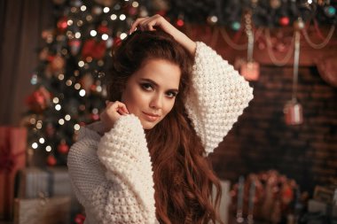 Noel örme kollu çekici kadın portresi. Güzel esmer kız uzun saç stili ile Noel ağacı ve xmas hediye süslemeleri üzerinde sıcak beyaz yün kazak giyer.