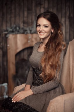 Rahat iç gri elbiseli karanlık uzun kıvırcık saçlı Genç neşeli güzel kız portresi kapatın. Kamera seyir ile mutlu ve rahat yüz ifadesi ile gülümseyen esmer.