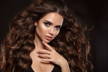 Uzun kahverengi kıvırcık saçlı güzel kadın. Portre portre ile genç kızın güzel bir yüz. Stüdyoda poz izole üzerinde siyah arka plan moda modeli ile manikür çivi.