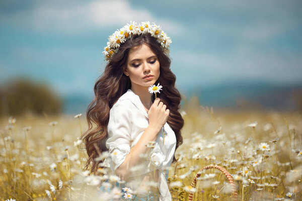 Beautiful young girl with flower enjoying in chamomile field. Carefree happy brunette woman with chaplet on healthy wavy hair having fun outdoor in nature. People freedom style.