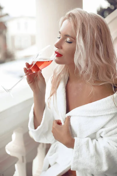 Beautiful blond bride woman in white bath robe enjoying glass of — Stock Photo, Image