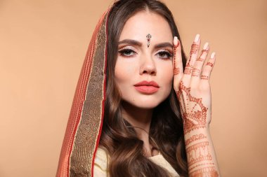 Mehendi. Bej üzerine izole edilmiş sari giymiş güzel Hintli kız portresi. Kundan altın mücevher setiyle genç Hindu kadın model. Geleneksel Hint kostümü lehenga choli. Elinde kına resmi var..