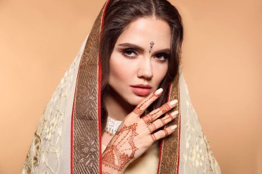 Mehendi. Bej üzerine izole edilmiş sari giymiş güzel Hintli kız portresi. Kundan altın mücevher setiyle genç Hindu kadın model. Geleneksel Hint kostümü lehenga choli. Elinde kına resmi var..
