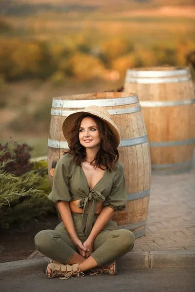 公园里坐在木桶边的美丽女人的画像 戴着卷曲的帽子 脸上挂着笑容 秋日落日照片 — 图库照片