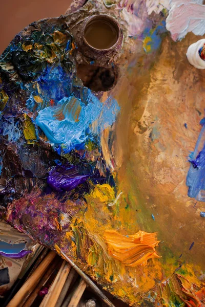 Palette artist table workplace for mixing oil paint. Close-up tools with tubes and brushes. Mix colors mess chaos real life. Creative atmosphere. Artist\'s Studio draw