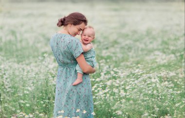 Anne ve çocuğu yazın papatya tarlasında. Anne sevgisi şefkati bakımı. Annelik duygusal olarak mutluluktur. Doğal eko. Anneler Günü. Güzel bir kız bebek. Uyum. Köy hayatı 