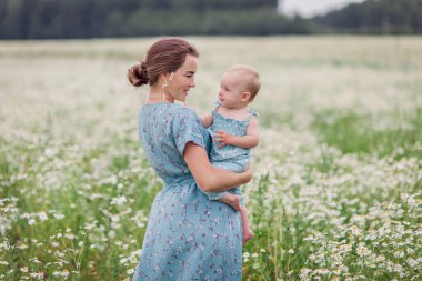 Anne ve çocuğu yazın papatya tarlasında. Anne sevgisi şefkati bakımı. Annelik duygusal olarak mutluluktur. Doğal eko. Anneler Günü. Güzel bir kız bebek. Uyum. Köy hayatı 