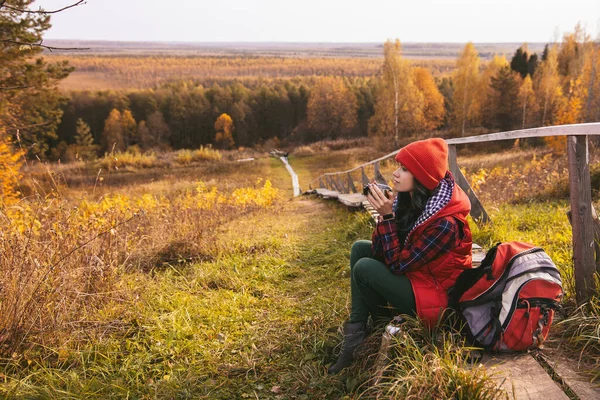 woman is resting in the autumn forest. Fall mood to travel. Colorful beautiful natural landscape. Drinks from a thermos. Loneliness freedom silence melancholy. Cozy dreams. Hiking tourism leisure.