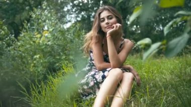 Genç bir kadın çimenlerde oturuyor.