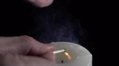 Siyah arkaplanda çok yavaş çekimde kibritle mum yakılıyor
