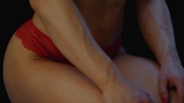 Siyah deri üzerinde çiy damlaları olan, kırmızı iç çamaşırlı genç bir kadının gövdesi.