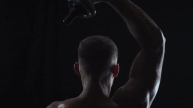 Genç, formda adam dambıl, siluet ve ağır çekimde triseps yapıyor.