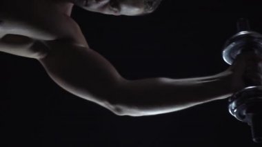 Tek elle dambıl, siluet ve ağır çekimde ağırlık kaldıran genç adam.