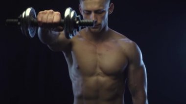 Genç, formda adam dambıllarla omuz egzersizi yapıyor, ağır çekim.