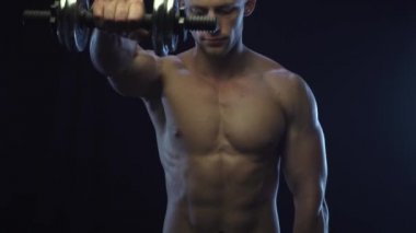 Genç, formda adam dambıllarla omuz egzersizi yapıyor, ağır çekim.