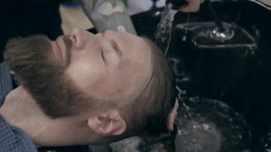 Berber dükkanında sakallı, genç ve yakışıklı bir adam. 100 fp 'den 25fps' ye kadar ağır çekimde. Saç yıkama işlemi