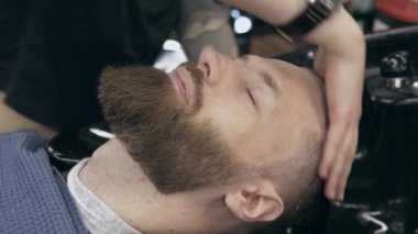 Berber dükkanındaki yakışıklı sakallı genç adam, sığ bir tarlada. Saç yıkama işlemi