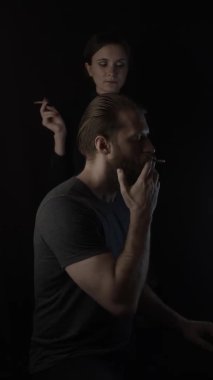 Siyahta sigara içen adam ve kadın. Dikey video. Yavaş çekim