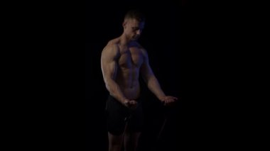 Siyah arka planda elastik bantlarla ön omuz egzersizi yapan genç adam. Ağır çekim. Yavaşça yakınlaştır