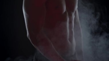 Bisepslerini gösteren dumandaki genç ve zinde bir adamın silueti. Yavaş çekim, dikey döndürme